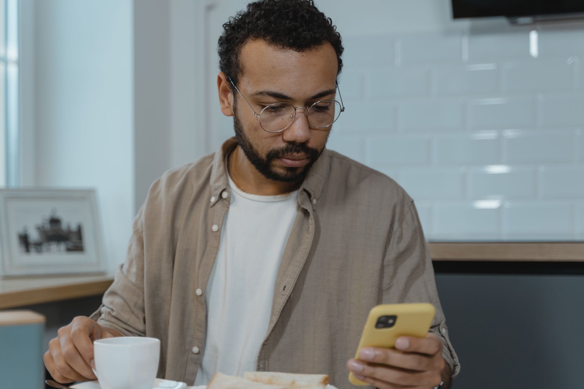 Un uomo con gli occhiali guarda lo smartphone mentre fa colazione in casa